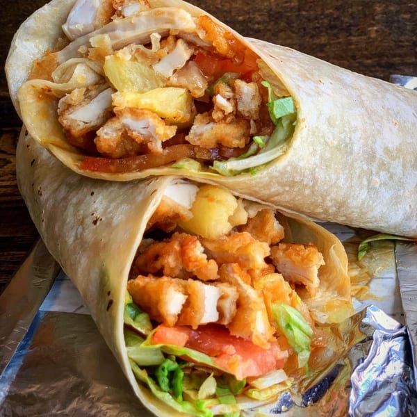 Two chicken wraps with lettuce, tomato, and pineapple, partially unwrapped on foil.