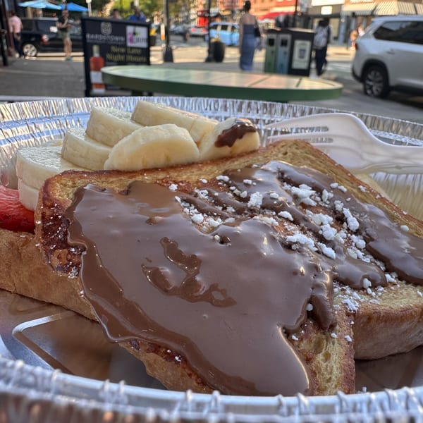 French toast with chocolate sauce, powdered sugar, bananas, and strawberries in a foil container.